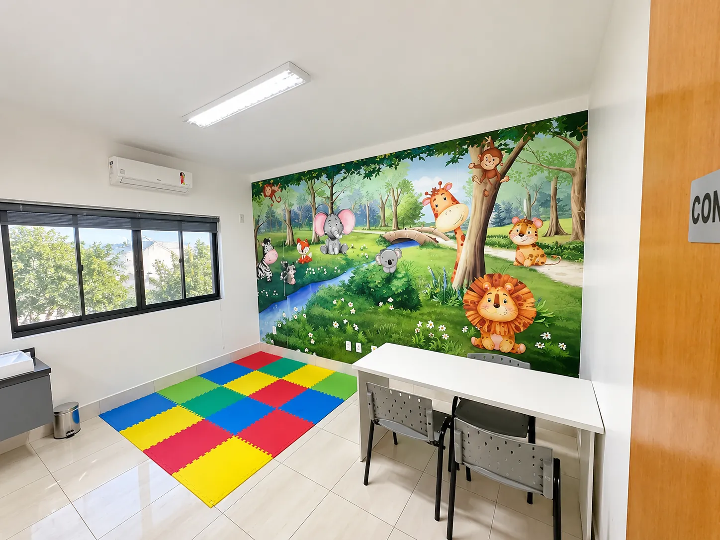 Sala de atendimento com mural da floresta, mesa e tapete de EVA colorido