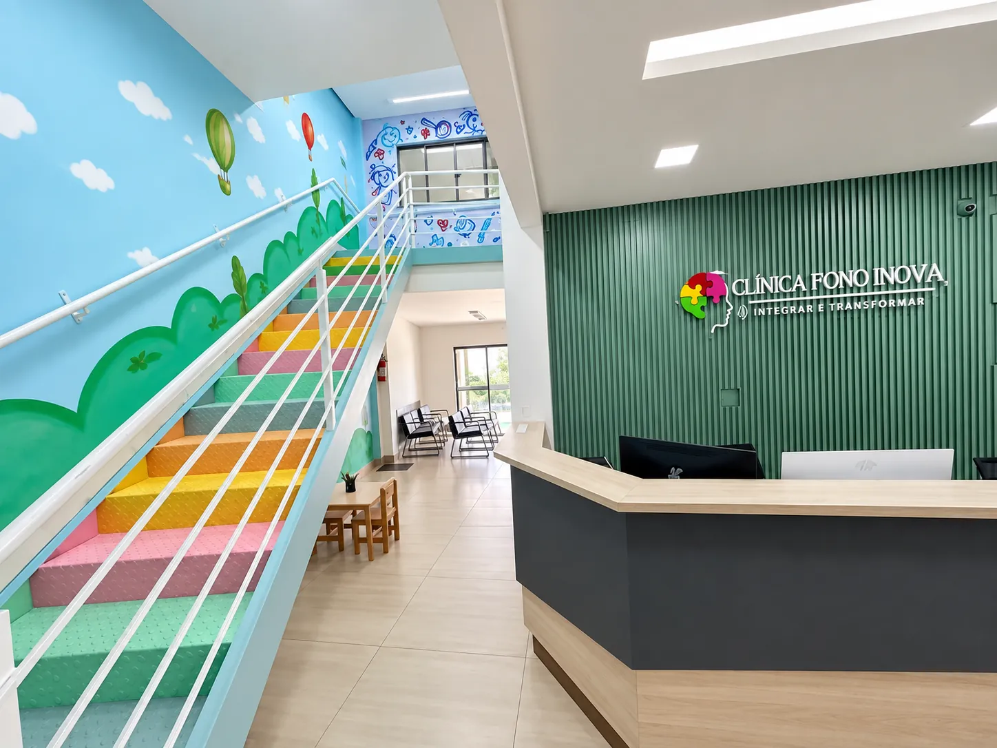 Recepção da Clínica Fono Inova com parede verde, escada colorida ao fundo e sala de espera